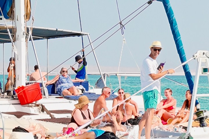 People relaxing on a catamaran in clear turquoise water on a sunny day.