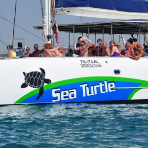 People on a boat named 'Sea Turtle' with a turtle logo, waving and enjoying the sunny day.