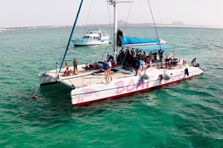 People on a catamaran labeled 'Boat Tour' in a turquoise sea, with another boat in the background.