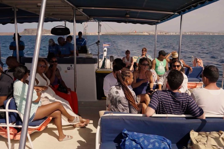 Group of people sitting on a boat with a covered roof, sailing in calm waters.