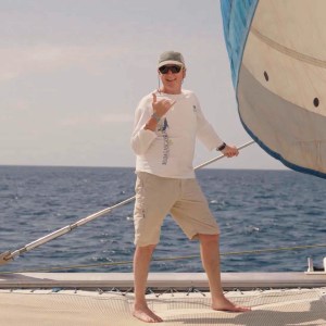 Person on a sailboat deck, holding a rope with the ocean in the background.