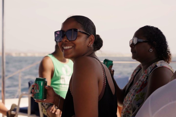 People on a boat holding drinks, smiling, wearing sunglasses.
