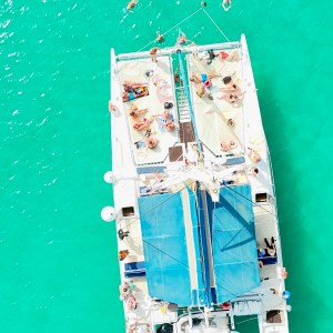 Catamaran with people in turquoise water, swimmers nearby.